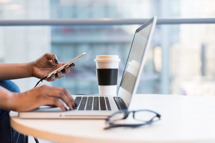 Person using a laptop with one hand and a mobile phone with the other