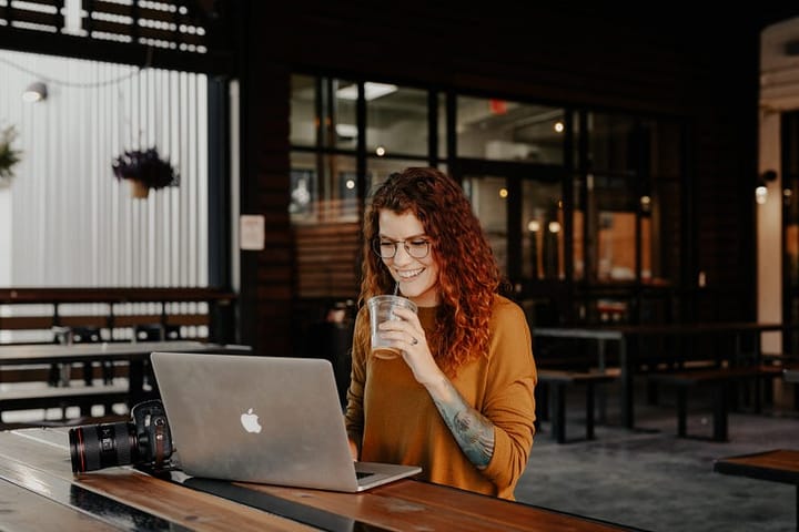 Woman with red hair sipping an iced coffee while using a computer